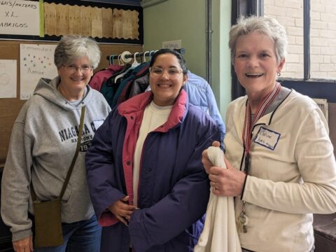 Laura Larson (l) and Celine Woznica (r) with a migrant volunteer trying on a coat.