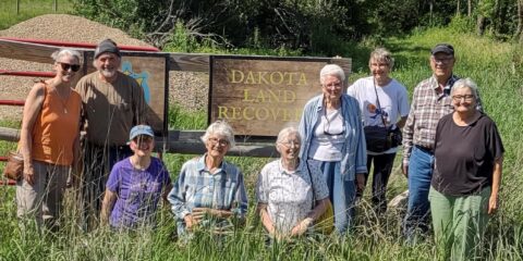 Nine people posing in front of sign that says "Dakota Land Recovery."